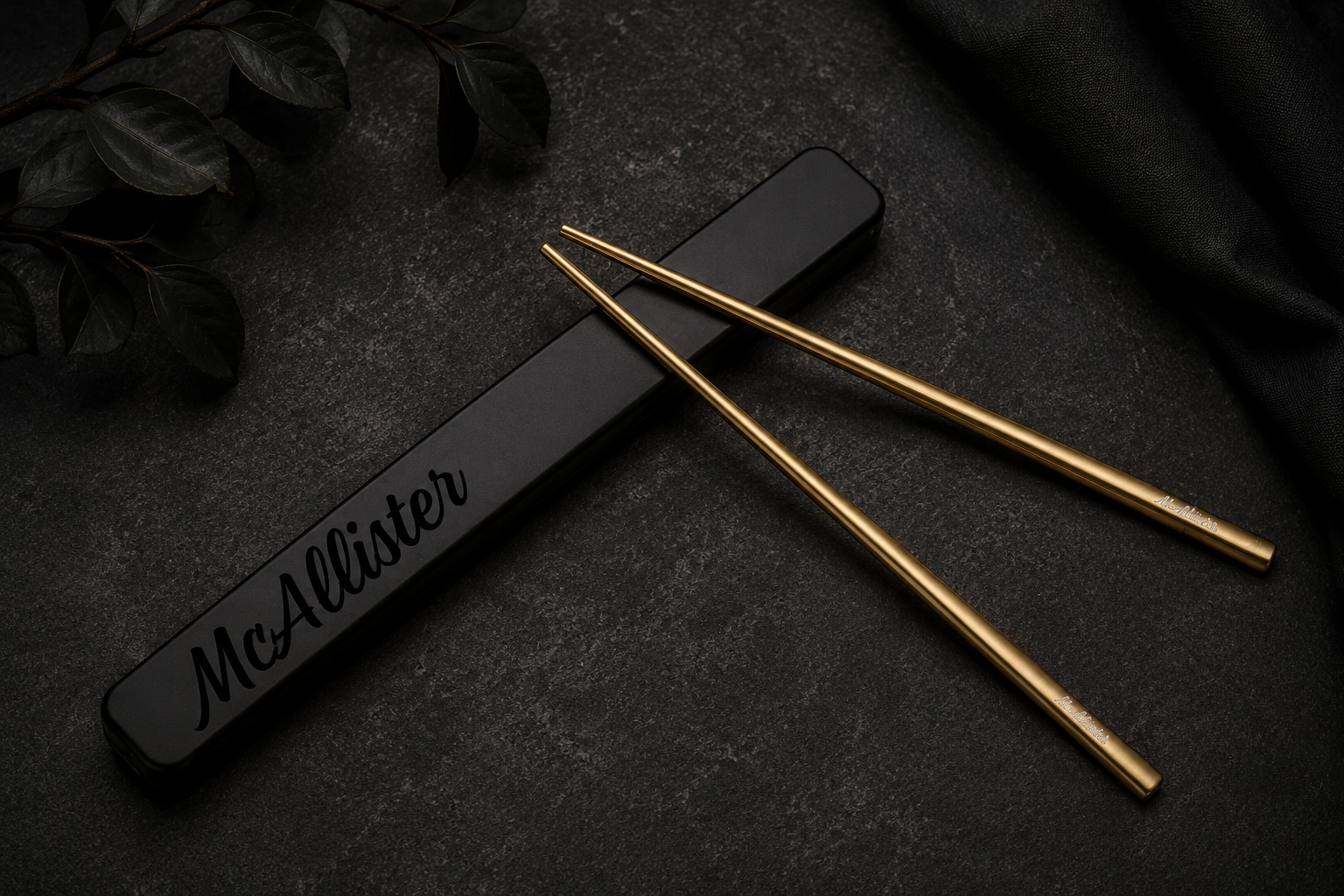 Personalized engraved stainless steel chopsticks with black storage case on a dark stone background